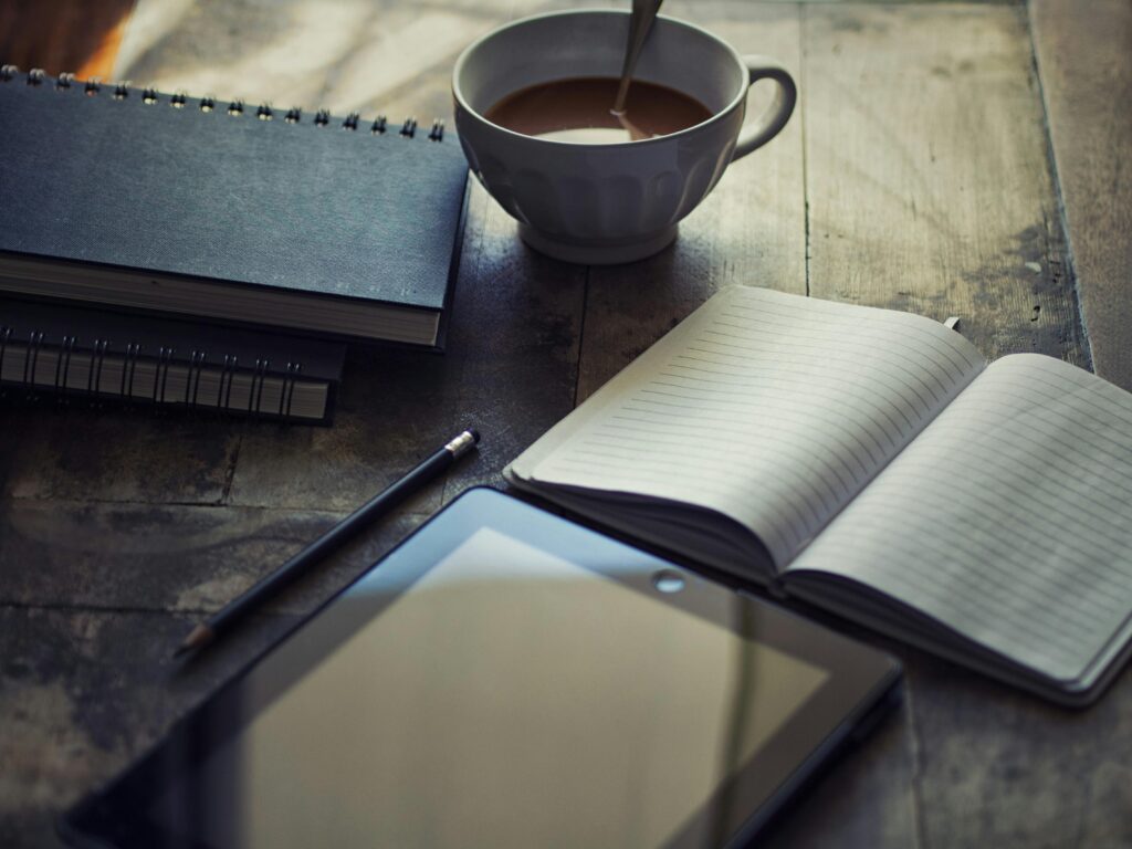 A cozy workspace setup with coffee, notebook, and tablet on a wooden table.